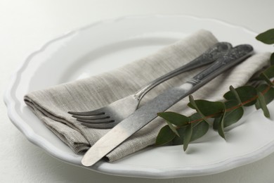 Photo of Stylish setting with cutlery, eucalyptus leaves and plate on white textured table, closeup