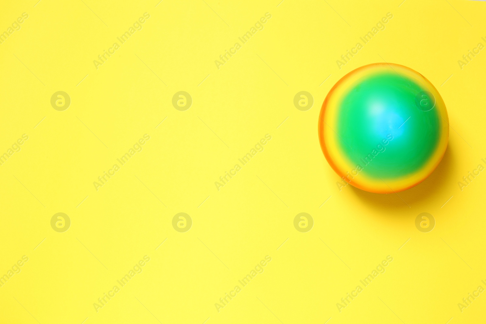 Photo of New bright kids' ball on yellow background, top view. Space for text