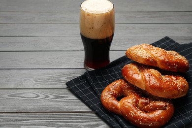 Photo of Tasty freshly baked pretzels with glass of dark beer on grey wooden table. Space for text
