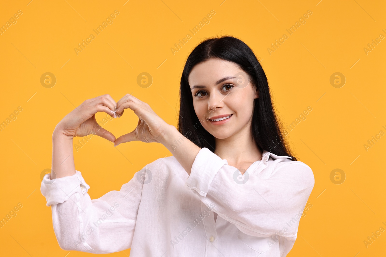 Photo of Smiling woman showing heart gesture with hands on orange background