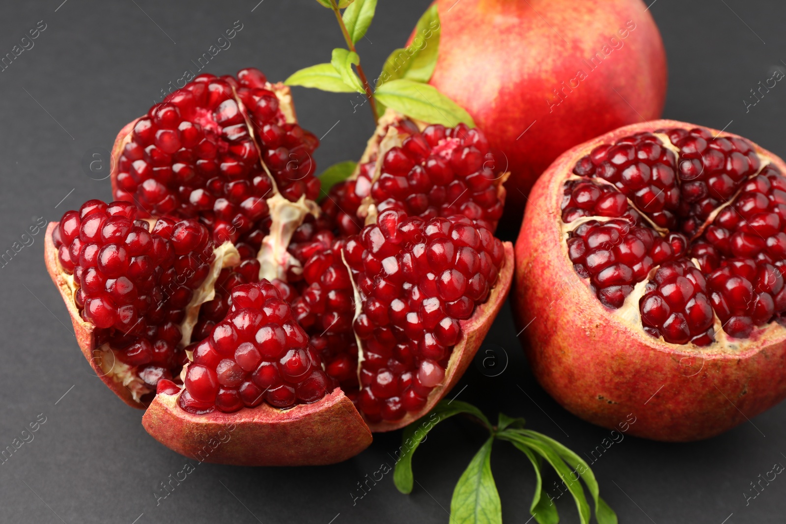 Photo of Fresh ripe pomegranates and leaves on grey background, closeup