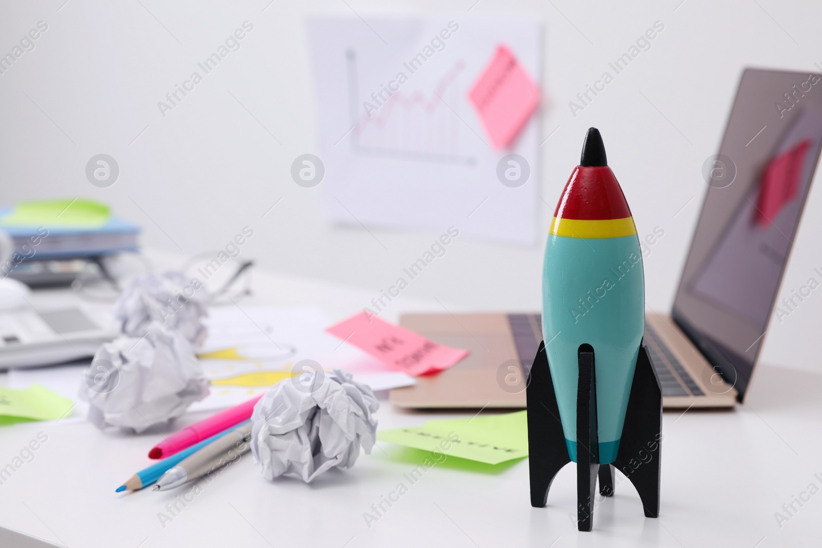 Photo of Toy rocket, laptop and crumpled paper on messy table indoors, space for text. Startup concept