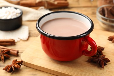 Photo of Tasty hot chocolate in cup and spices on wooden table, closeup