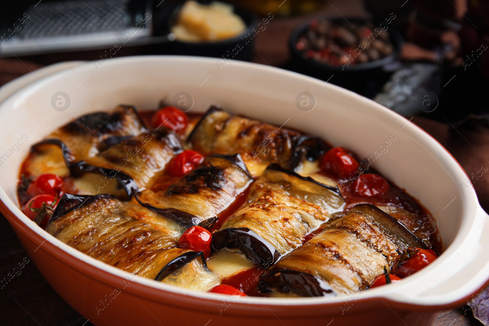 Photo of Tasty eggplant rolls with tomatoes and cheese in baking dish on table, closeup