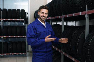 Photo of Male mechanic near rack with tires in auto store