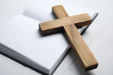 Photo of Christian cross and Bible on white wooden background, closeup. Religion concept