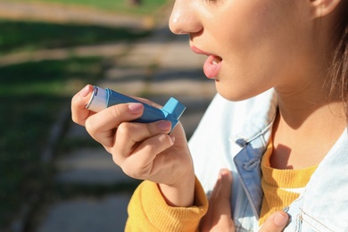 Photo of Woman using asthma inhaler outdoors. Health care