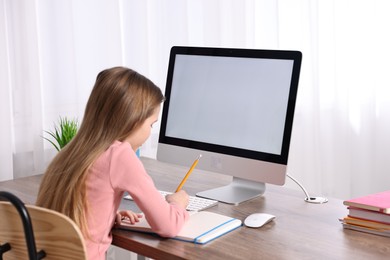 Photo of E-learning. Cute girl taking notes during online lesson at table indoors