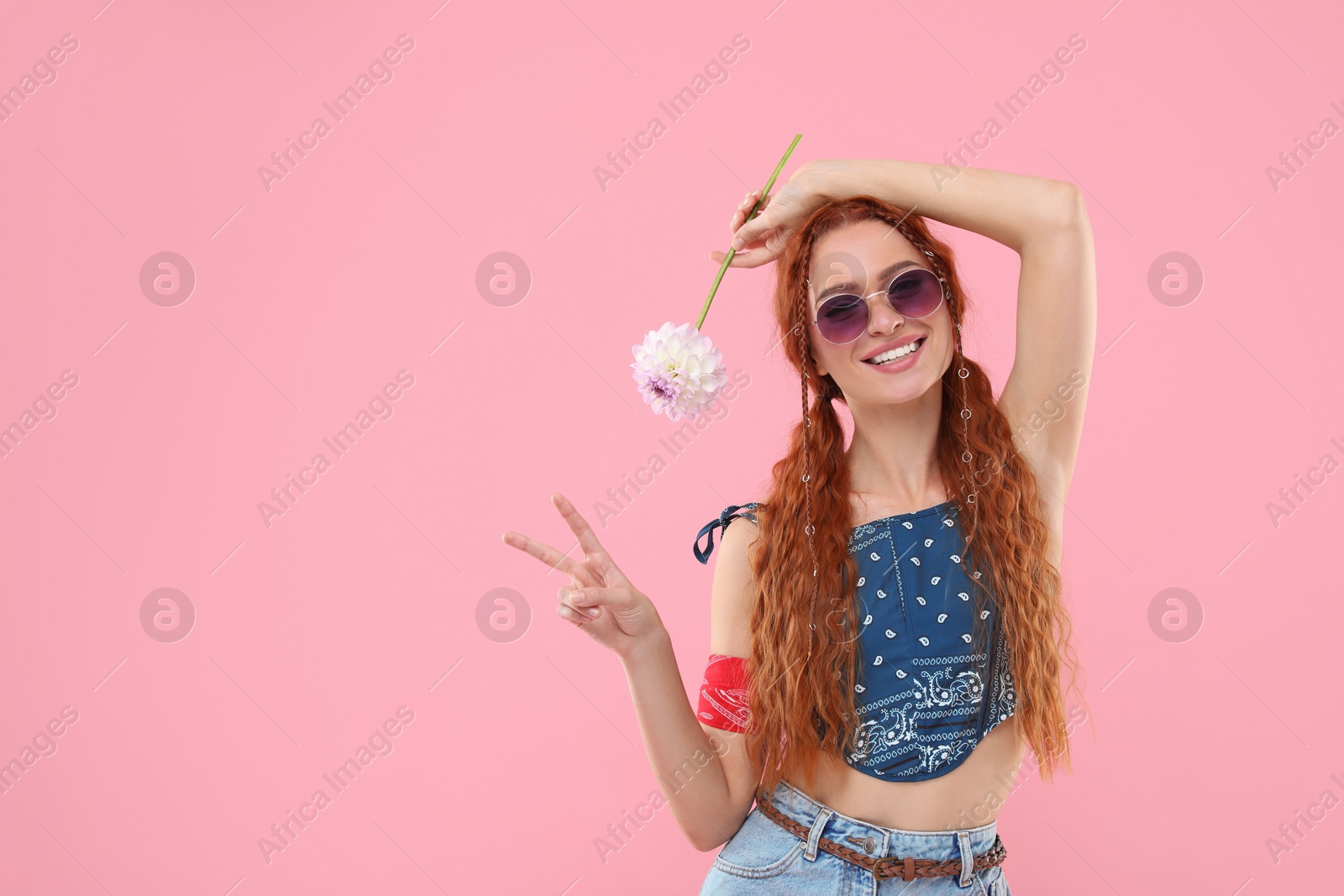 Photo of Stylish young hippie woman with dahlia flower showing V-sign on pink background, space for text