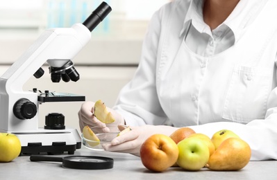 Photo of Scientist taking slice of apple at table in laboratory, closeup. Poison detection