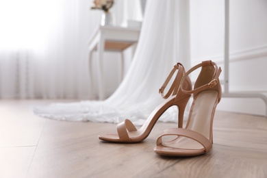 Photo of High heeled shoes and wedding dress in room, closeup
