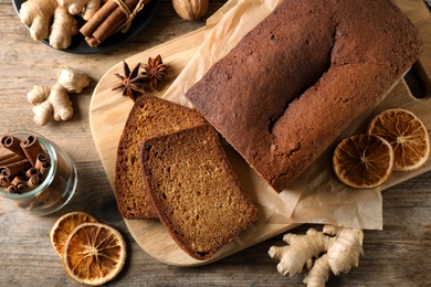 Photo of Delicious gingerbread cake and ingredients on wooden table, flat lay