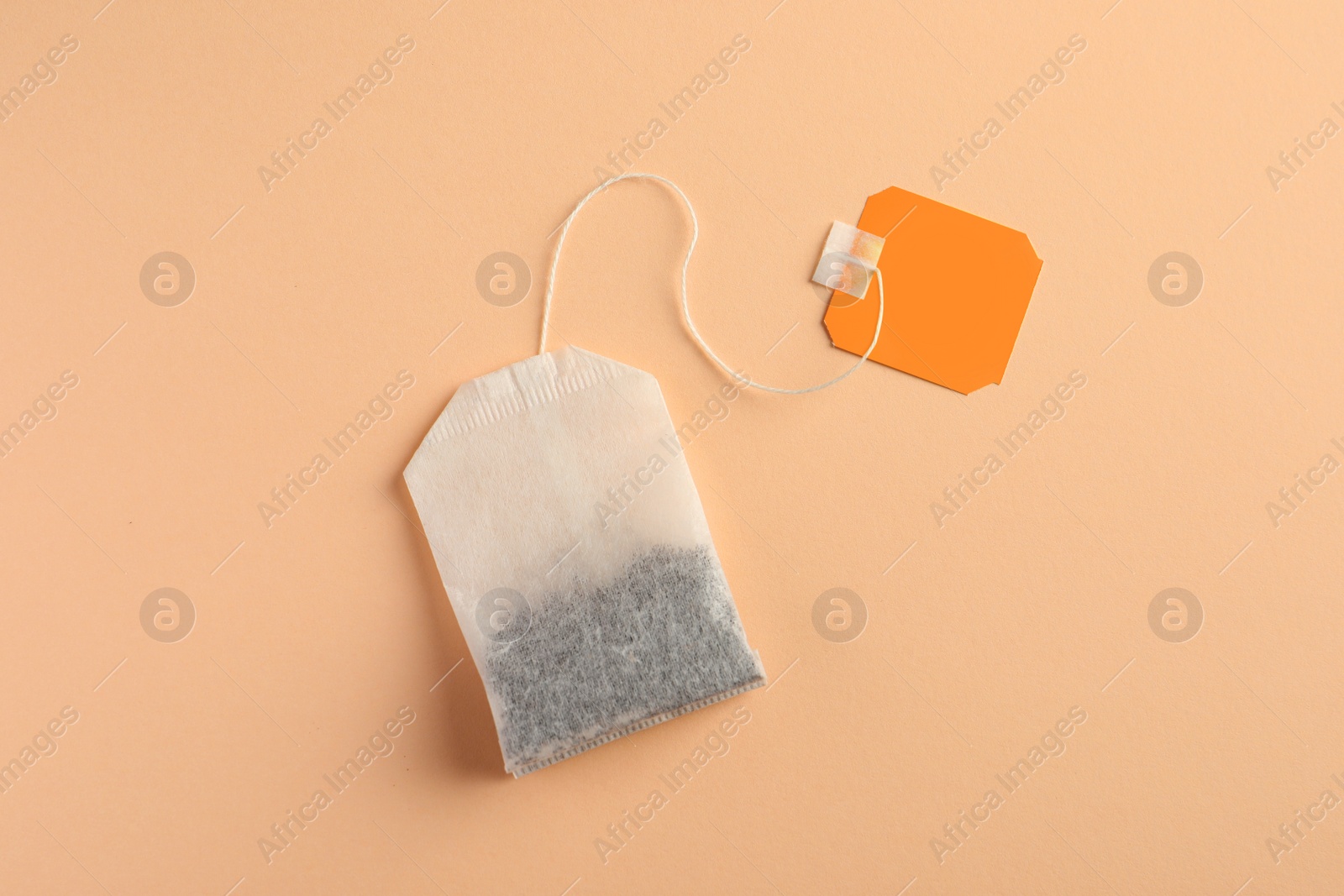 Photo of New tea bag with tab on pale orange background, top view