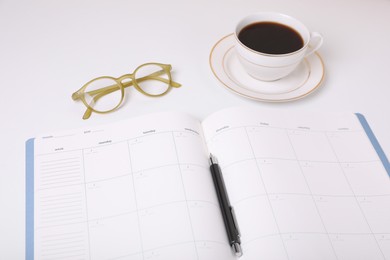 Photo of Open monthly planner, coffee, glasses and pen on white background