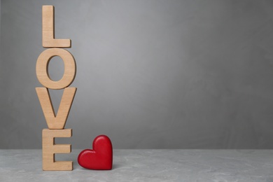 Photo of Word Love made of wooden letters near red decorative heart on light grey table. Space for text