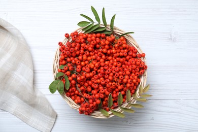 Photo of Fresh ripe rowan berries and leaves in wicker basket on white wooden table, top view