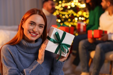 Photo of Christmas celebration in circle of friends. Happy young woman with gift box at home, selective focus