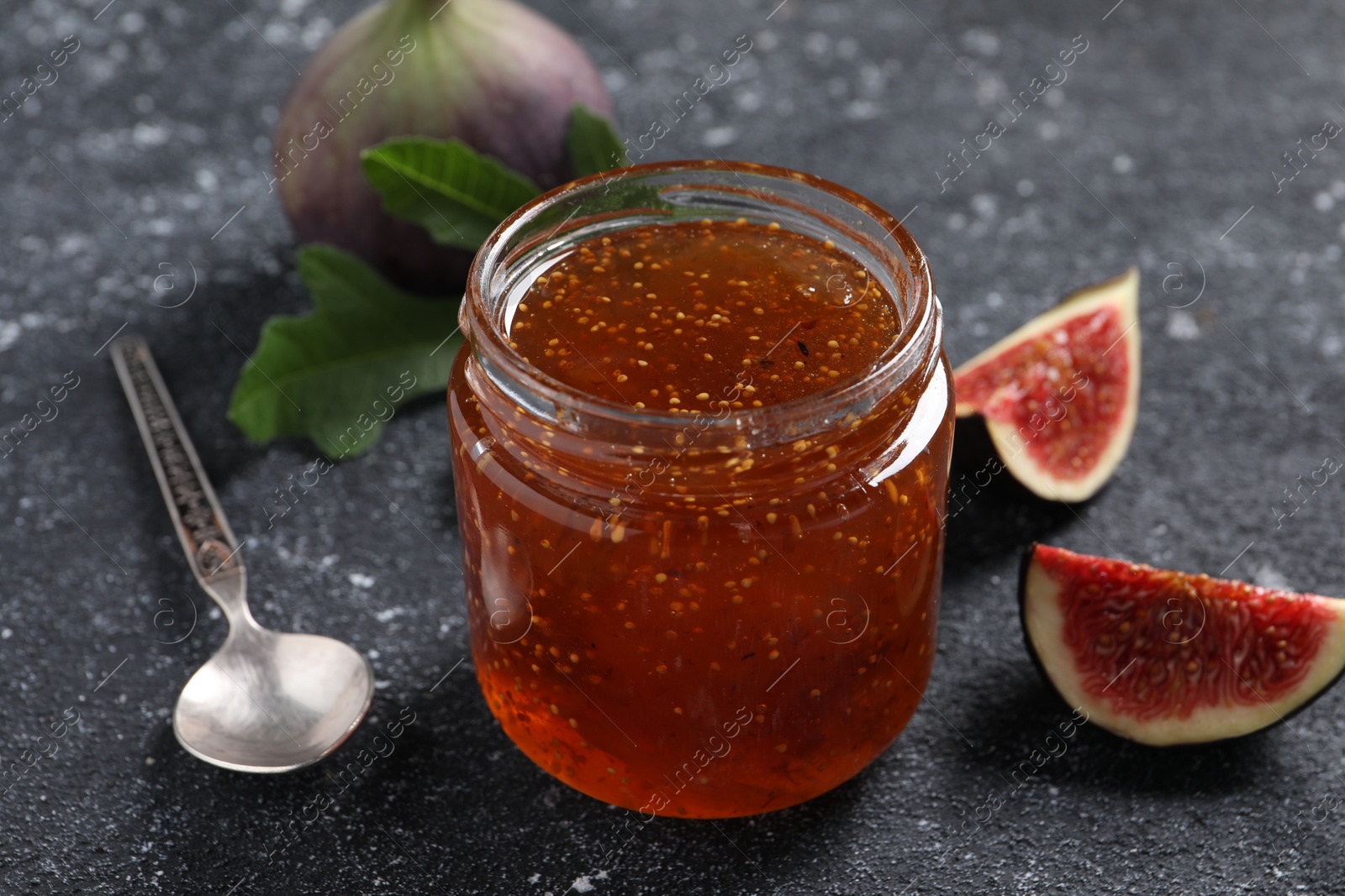 Photo of Jar with tasty sweet jam, fresh figs and spoon on black textured table, closeup