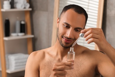 Photo of Handsome man with cosmetic serum in hands in bathroom, space for text
