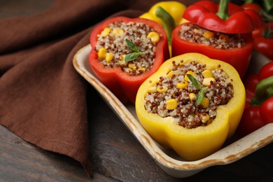 Photo of Quinoa stuffed bell peppers and basil in baking dish on wooden table, closeup. Space for text