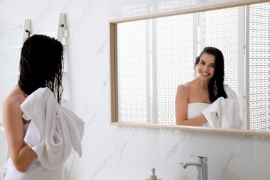 Photo of Happy young woman drying hair with towel after washing near mirror in bathroom