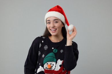 Photo of Happy young woman in Christmas sweater and Santa hat on grey background