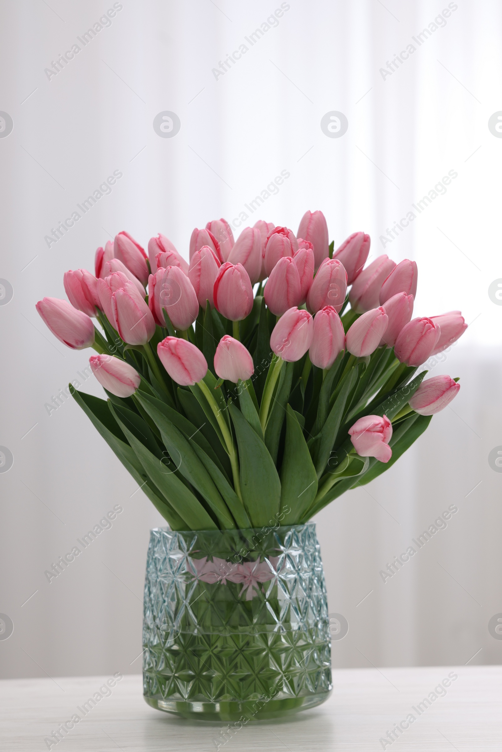 Photo of Bouquet of beautiful pink tulips in vase on white wooden table indoors