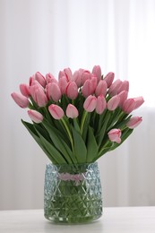 Bouquet of beautiful pink tulips in vase on white wooden table indoors