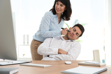 Photo of Young woman drawing on colleague's face while he sleeping at workplace. April fool's day