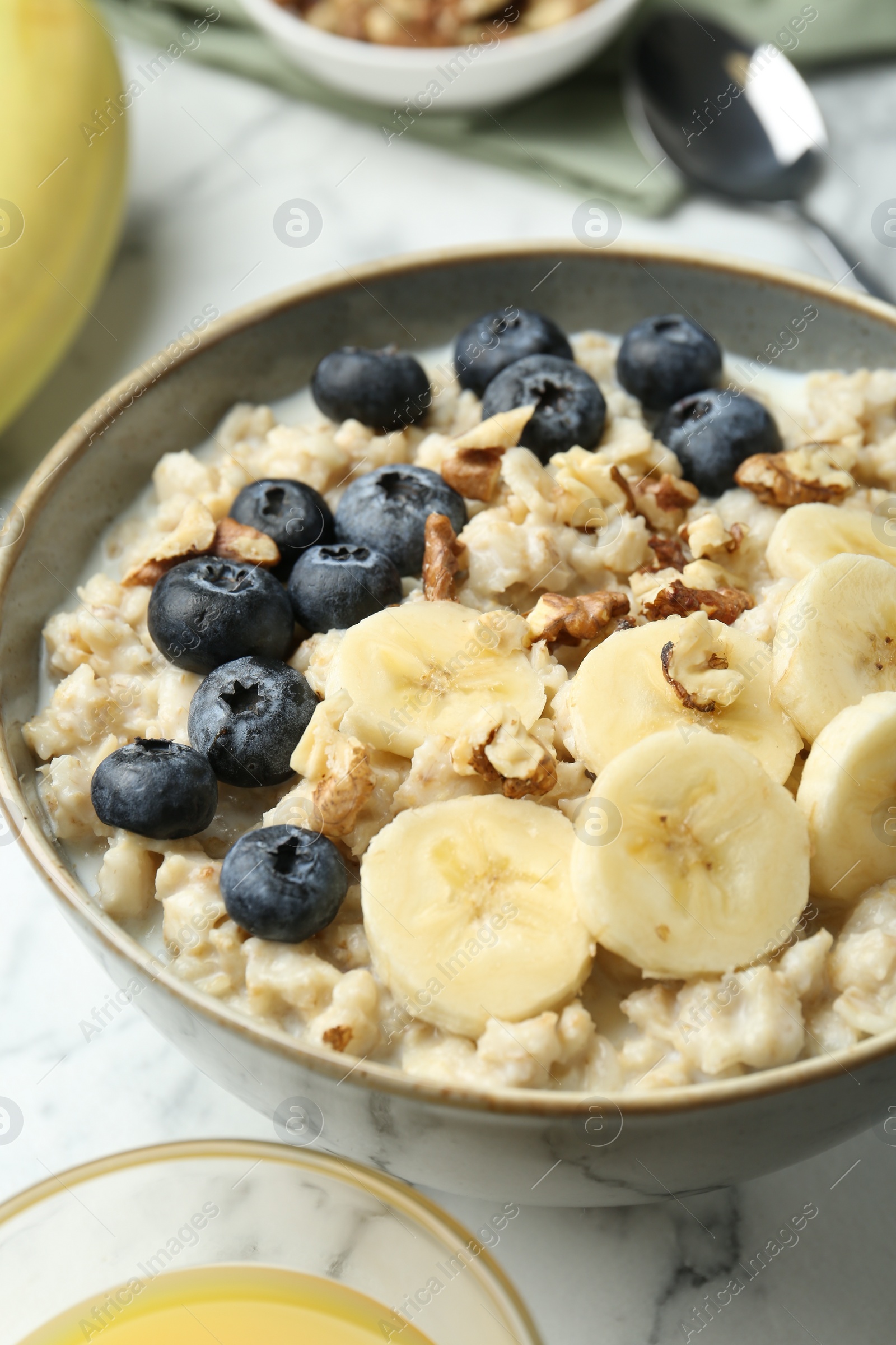 Photo of Tasty oatmeal with banana, blueberries, walnuts and milk served in bowl on white marble table, closeup