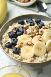 Photo of Tasty oatmeal with banana, blueberries, walnuts and milk served in bowl on white marble table, closeup