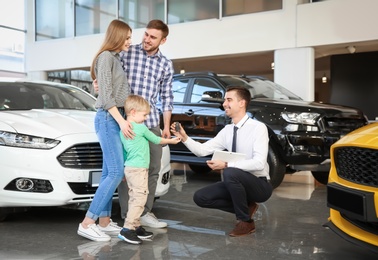 Photo of Salesman giving car key to young family in salon