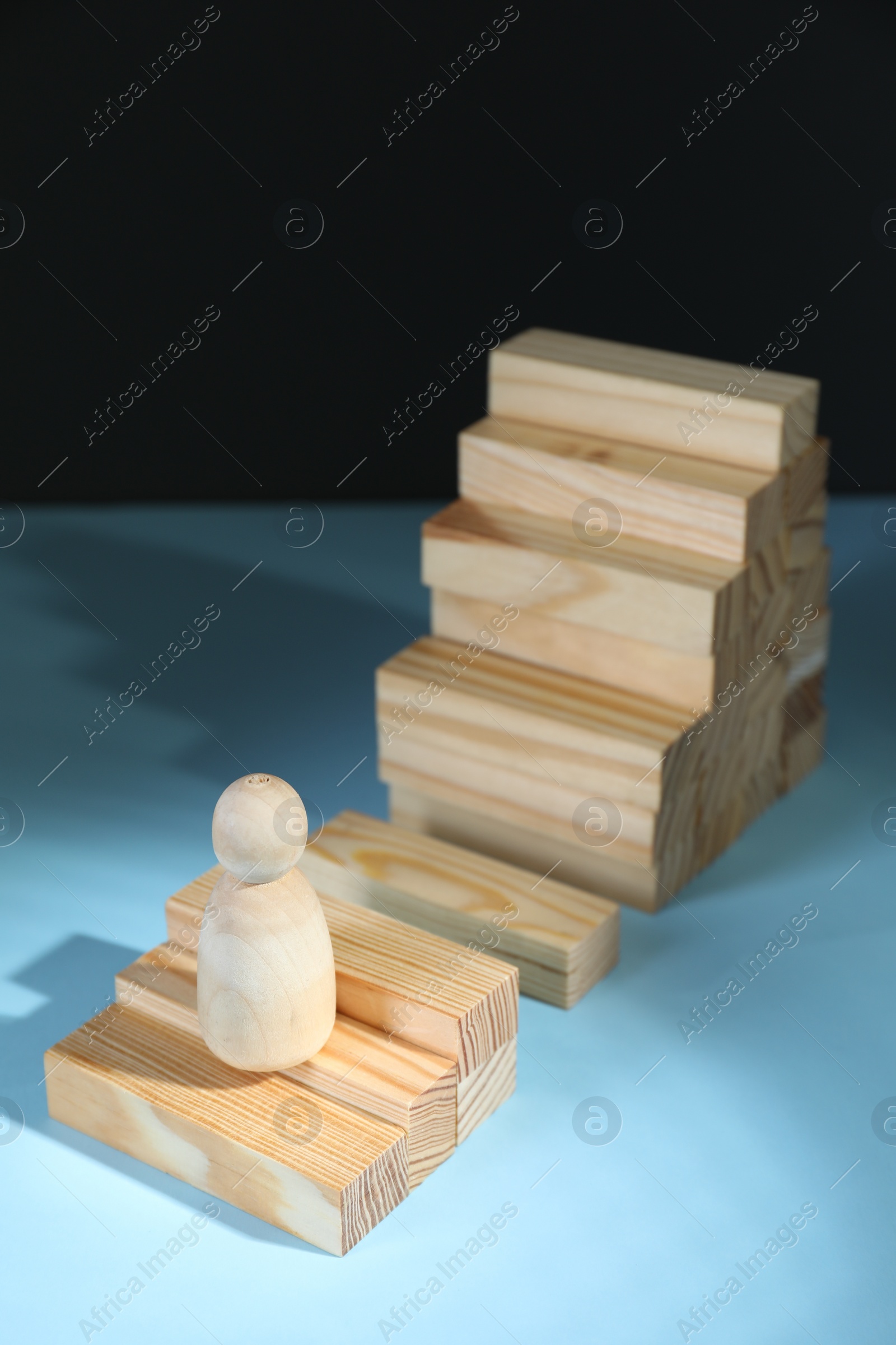 Photo of Stairs of blocks with gap as barrier and wooden human figure on light blue surface. Path to growth and success