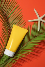 Sunscreen, starfish and tropical leaves on coral background, flat lay. Sun protection care