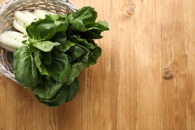 Fresh green pak choy cabbages in wicker basket on wooden table, top view. Space for text