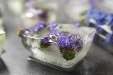 Photo of Ice cube with flowers on grey stone table, closeup