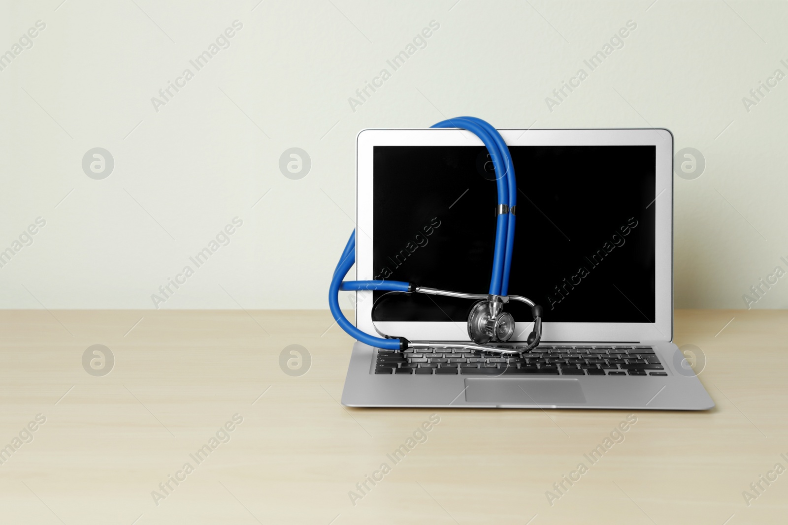 Photo of Laptop with blank screen and stethoscope on table against light background, space for text. Computer repair