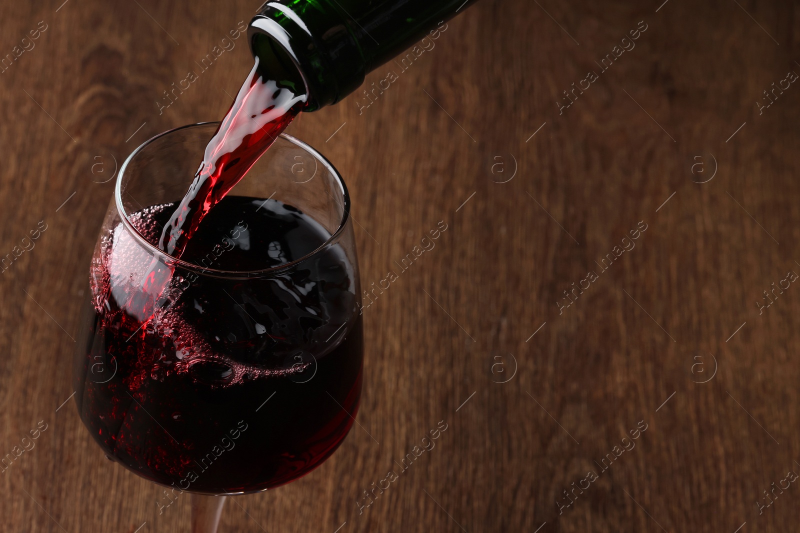 Photo of Pouring tasty red wine in glass at wooden table, closeup. Space for text
