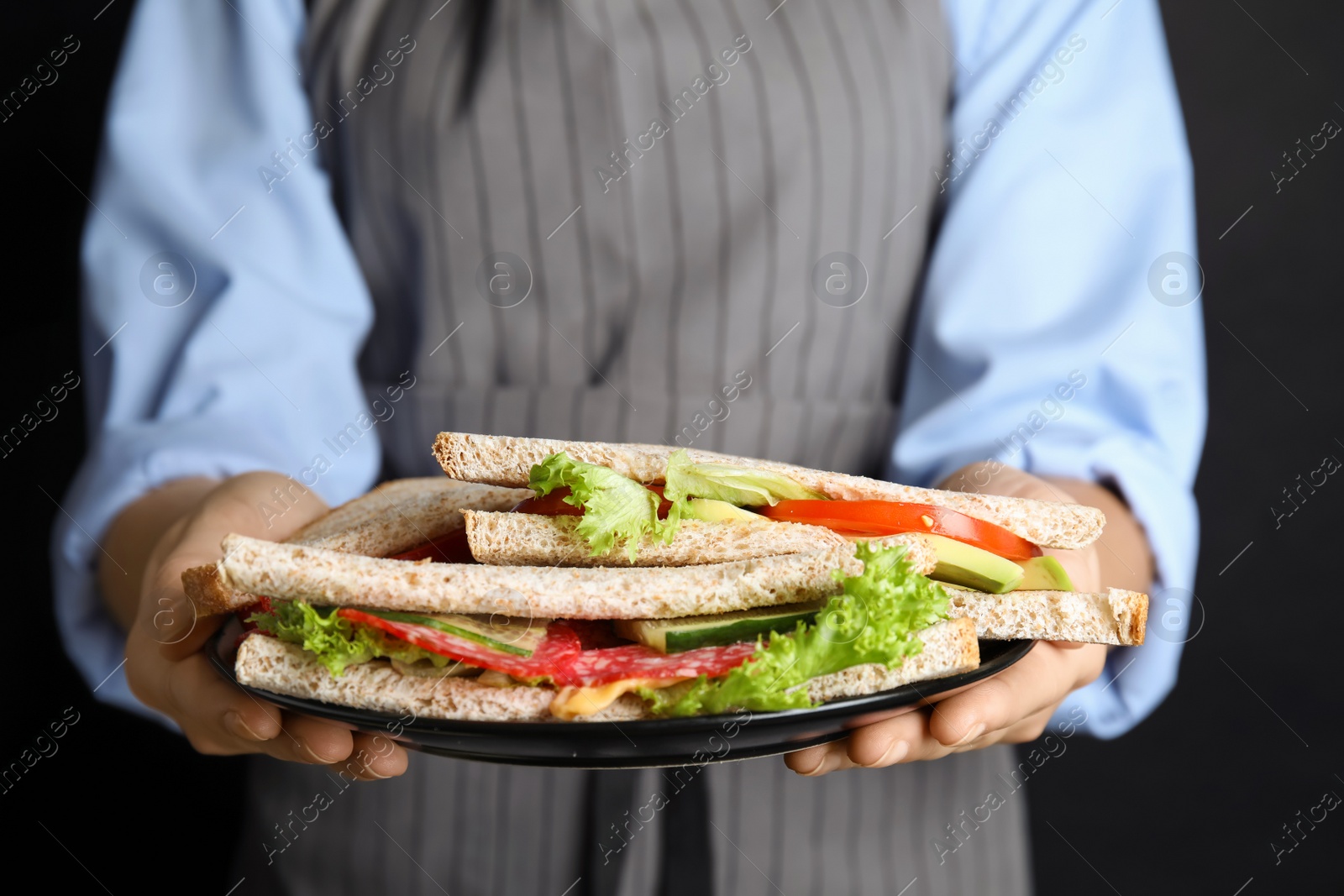 Photo of Woman holding plate with tasty sandwiches on black background, closeup