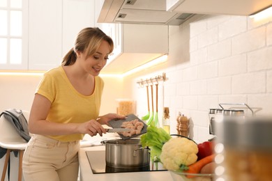 Woman putting meat into pot to make bouillon in kitchen. Homemade recipe