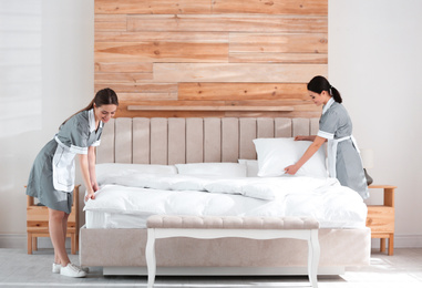 Young chambermaids making bed in hotel room