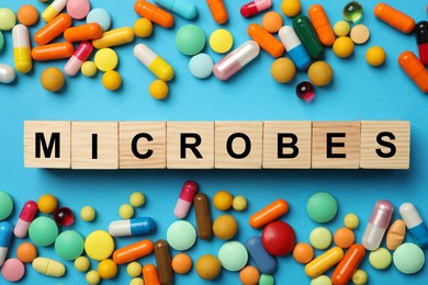 Photo of Word Microbes made with wooden cubes and pills on light blue background, flat lay