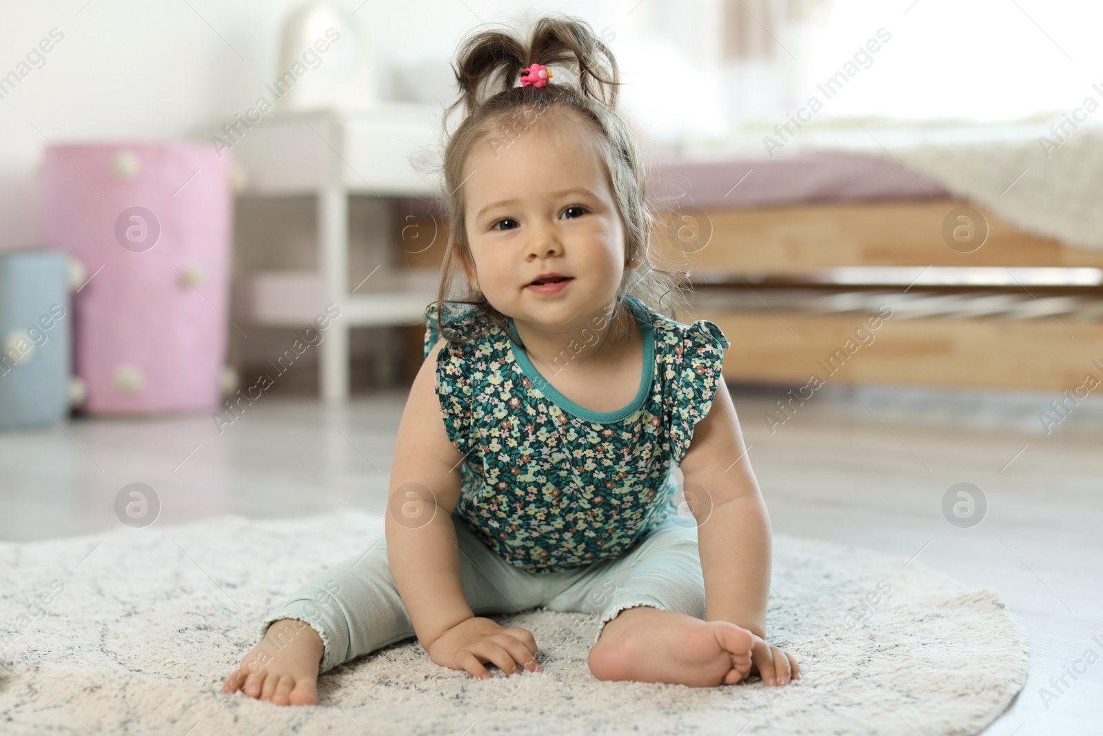 Photo of Adorable little baby girl sitting on floor in room