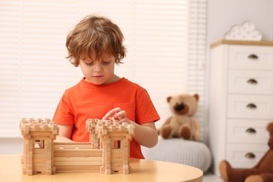 Photo of Cute little boy playing with wooden fortress at table in room, space for text. Child's toy