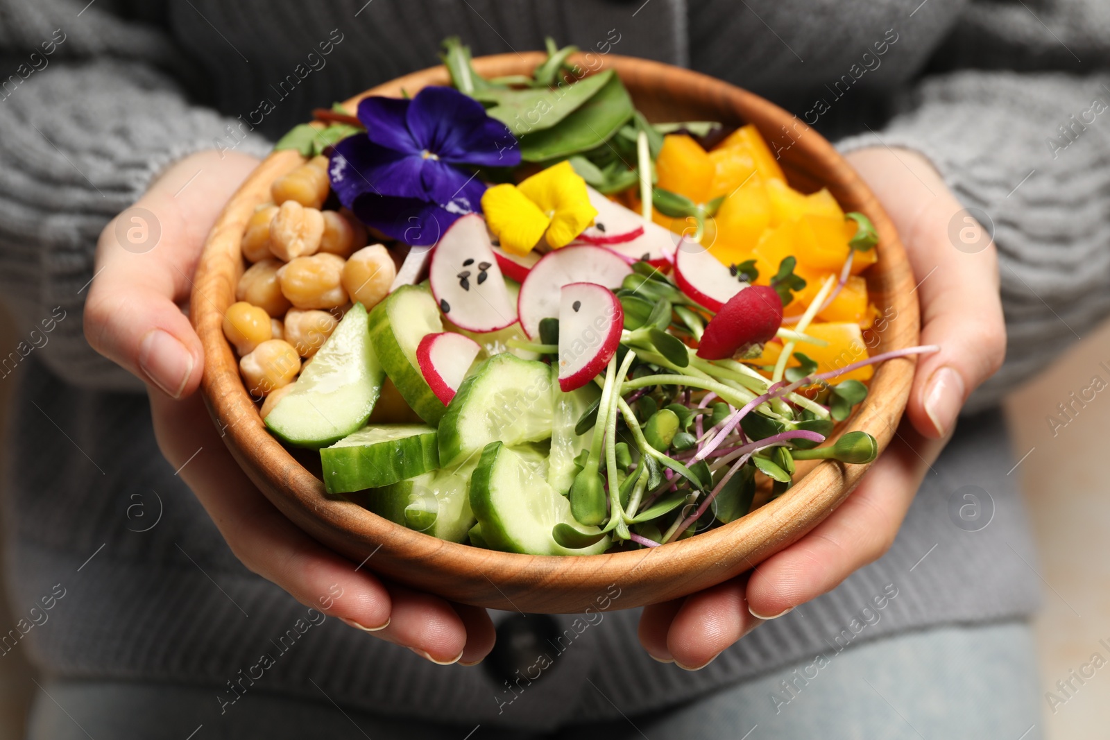 Photo of Woman holding delicious vegan bowl with cucumbers, chickpeas and violet flowers, closeup