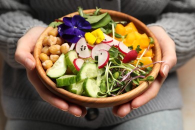 Woman holding delicious vegan bowl with cucumbers, chickpeas and violet flowers, closeup