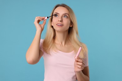 Photo of Beautiful woman applying mascara on light blue background