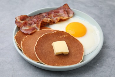 Photo of Tasty pancakes with fried egg and bacon on grey table, closeup