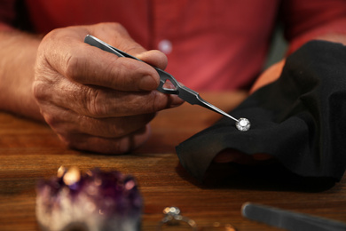 Photo of Professional jeweler working with beautiful gemstone at table, closeup