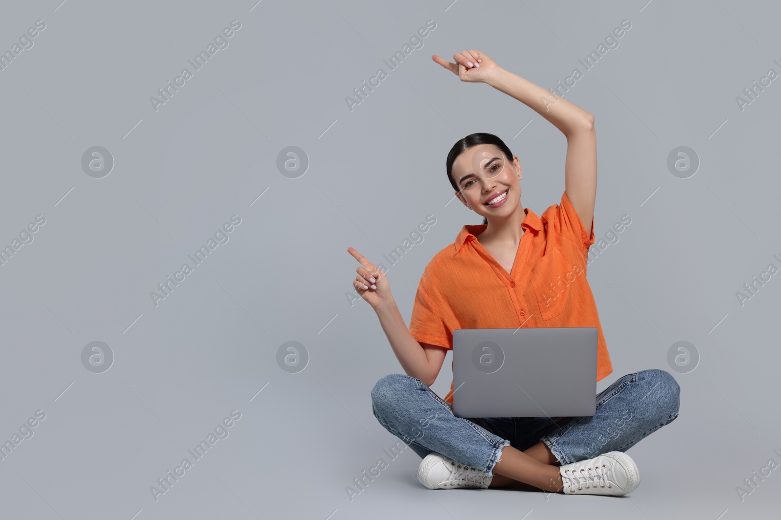 Photo of Happy woman with laptop pointing at something on light gray background, space for text